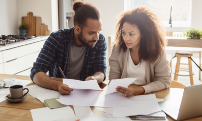 A stock photo of a person holding a stack of cash and looking at papers with the words "personal loan" written on them. The person is sitting at a desk in front of a computer. The image is meant to represent someone researching and considering taking out a personal loan.