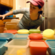 Image description: A neatly organized kitchen cabinet with various sizes and shapes of Tupperware containers arranged in rows, with their matching lids stacked nearby.