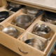 An image of neatly organized kitchen cabinets with dishes, cups, and utensils in designated spaces. The alt text could read: "A well-organized kitchen cabinet with plates, cups, and utensils arranged in their designated spaces. Tips for organizing kitchen cabinets include sorting items by frequency of use, using drawer dividers, and labeling containers."