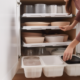 A neatly organized drawer filled with various sizes and shapes of Tupperware containers and lids, with the lids stacked neatly in a vertical row on the right side of the drawer.