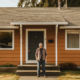 Image: A person holding a stack of papers and looking confused while standing in front of a house under construction. Alt text: A person seeking information for home renovation permits holds a stack of documents and stands in front of a house under construction.