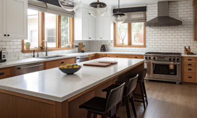 An image of a modern kitchen with sleek finishings, including a marble countertop, stainless steel appliances, and a large island with bar stools. The kitchen is well-lit and features open shelving to display decorative dishes and glassware.