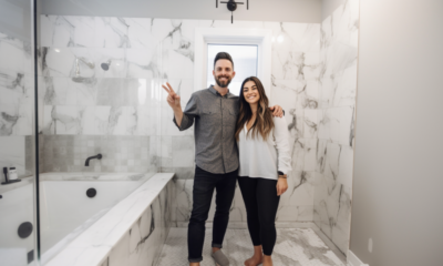 A bathroom with a newly renovated shower stall featuring large tiles, a rainfall showerhead, and a glass door. The vanity has a modern design with a white countertop and sleek metal hardware. The bathroom also features a new toilet and fresh coat of paint on the walls.